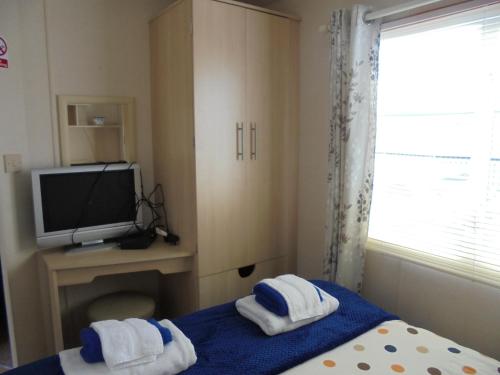 a bedroom with a bed and a tv and towels at 6 Berth on Golden Anchor (Cascade) in Chapel Saint Leonards