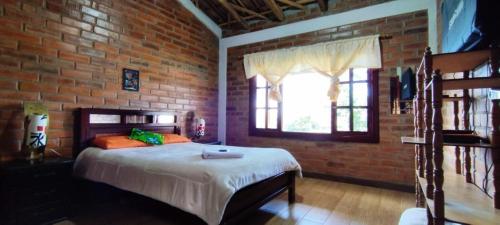 Dormitorio con paredes de ladrillo, cama y ventana en Cabaña San Andres, en Otavalo