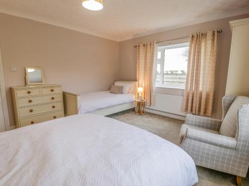 a bedroom with a bed and a chair and a window at Cynefin in Llandyfrydog