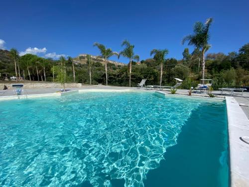 une grande piscine avec de l'eau bleue et des palmiers dans l'établissement Agriturismo L'impero Romano, à Gerace
