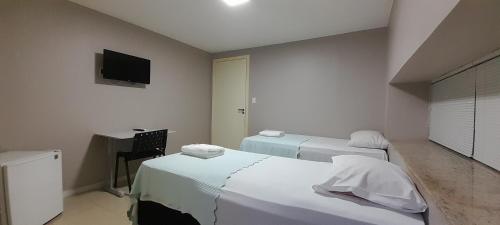Cette chambre comprend deux lits, un bureau et une télévision. dans l'établissement Pousada Kit Residence, à Brasilia
