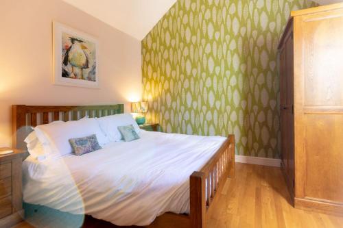 Cette chambre comprend un lit avec des draps blancs et du papier peint vert. dans l'établissement Grindle Cottage, à Woodbury