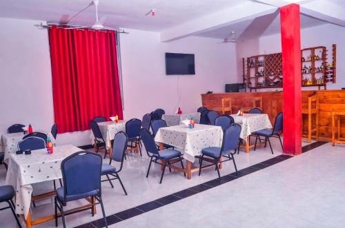 une salle à manger avec des tables et des chaises blanches et des rideaux rouges dans l'établissement Muhako Hotel, à Dar es Salaam