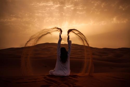 Una donna seduta nel deserto con le mani in alto di Mhamid Sahara Camp - Mhamid El Ghizlane a M'Hamid