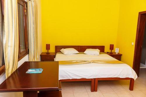 a bedroom with a bed with a table and yellow walls at Pousada Quinta Ribeirinha in Cidade Velha