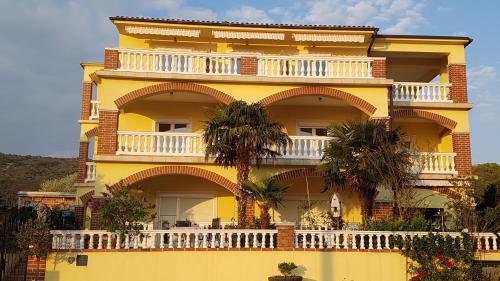 - un bâtiment jaune avec un balcon blanc et des palmiers dans l'établissement Bed & Breakfast Ružica, à Novi Vinodolski