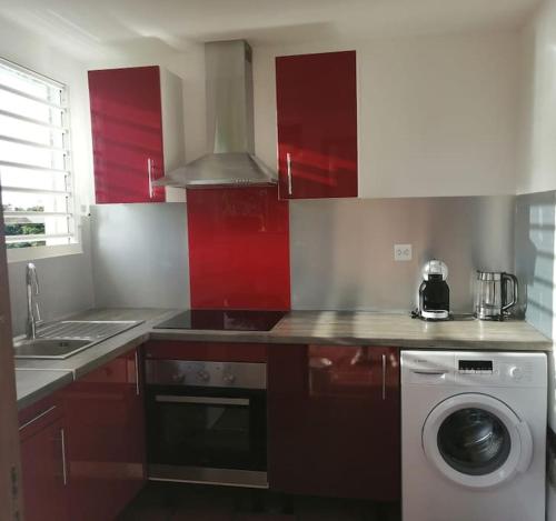 a kitchen with red cabinets and a washing machine at Duplex Rose Porcelaine - Vue Mer- Malendure in Bouillante