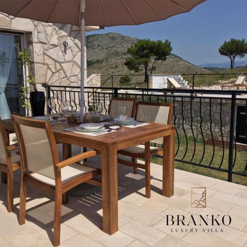 einen Holztisch mit Stühlen und einem Sonnenschirm auf einer Terrasse in der Unterkunft Villa Branko in Ravno