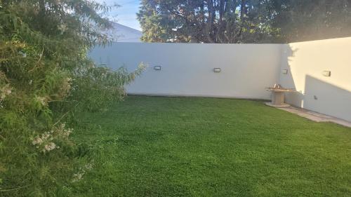 einen Hof mit einer weißen Wand und grünem Gras in der Unterkunft Gwyneth casa de playa in Puerto Madryn