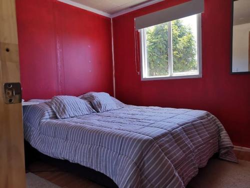 1 dormitorio con 1 cama con pared roja y ventana en Casa en parcela, en Puerto Varas