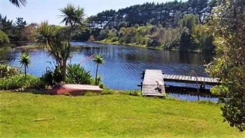 a bridge over a lake with a boat in the grass at The Lakes - Kai Iwi Lakes Exclusive Retreat in Kaihu