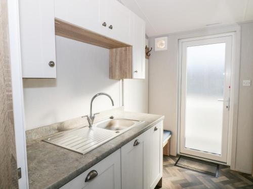 a white kitchen with a sink and a window at Dershel Lodge in Dumfries