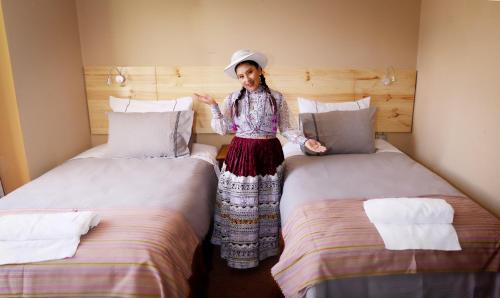 a woman standing between two beds in a room at Colibrí Inn in Chivay