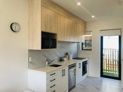 una cocina con armarios blancos y un reloj en la pared en Cozy Brand New Townhouse 24, en Auckland