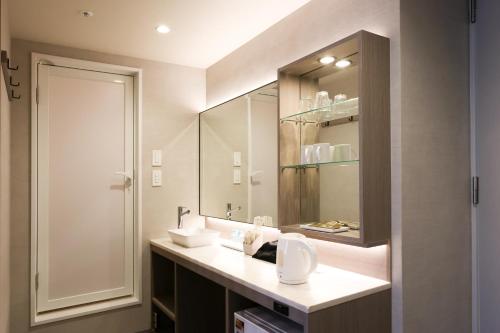 ein Bad mit einem Waschbecken und einem Spiegel in der Unterkunft SK HOTEL Kobe Ekimae in Kōbe