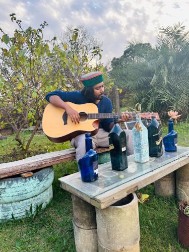 a man playing a guitar on a table at Dreamwoods A travellers farm in Dharamshala