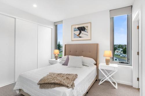 a white bedroom with a bed and two windows at Moana Esplanade - Pure Beach Front 3 Bed Apt in Moana