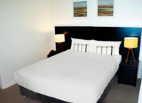 a bedroom with a large white bed with two lamps at Oshen Holiday Apartments Yeppoon in Yeppoon