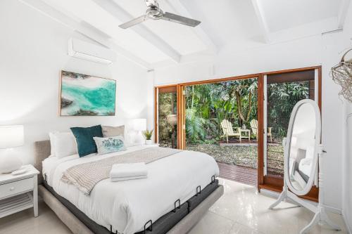 a white bedroom with a bed and a large window at Belle Escapes Tropical Haven Holiday Home Palm Cove in Palm Cove