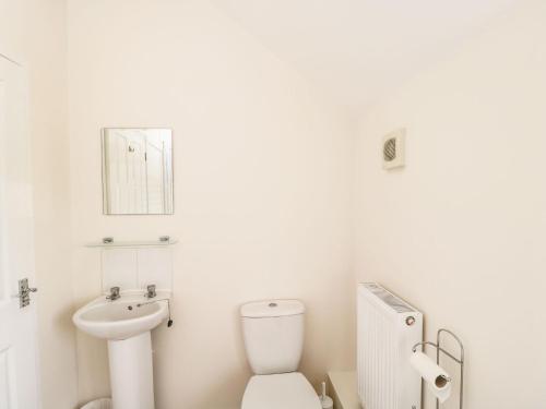 a white bathroom with a toilet and a sink at Stables Cottage in Melksham