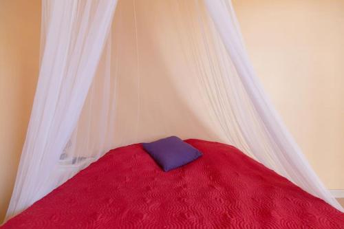 a bed with a red and white canopy with a blue pillow at Studio Colibri... Cap sur le Nord ! in Marigot