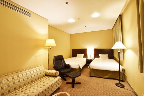 a hotel room with two beds and a couch at Hotel Nikko Tsukuba in Tsukuba
