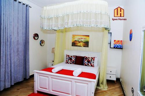 a small bedroom with a white bed with a red blanket at Igwe Homes - Kisaasi in Kampala
