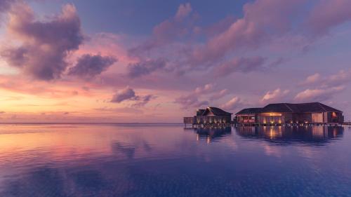 a couple of buildings on the water at sunset at Lily Beach Resort and Spa - All Inclusive in Dhangethi