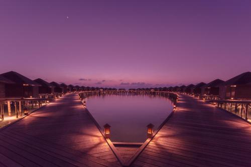 a boardwalk with lights in the water at night at Lily Beach Resort and Spa - All Inclusive in Dhangethi