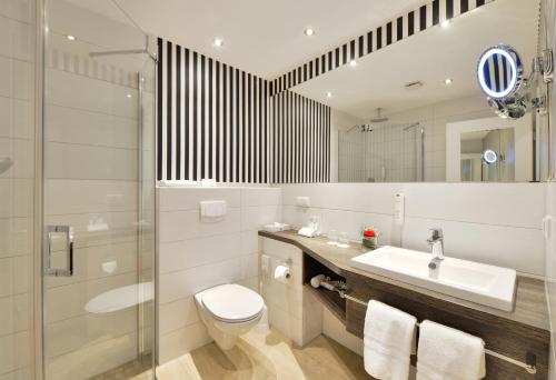 een badkamer met een wastafel, een toilet en een spiegel bij Ringhotel Landhaus Gardels in Sankt Michaelisdonn