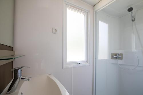 a bathroom with a sink and a shower with a window at Camping RCN Le Moulin de la Pique in Belvès