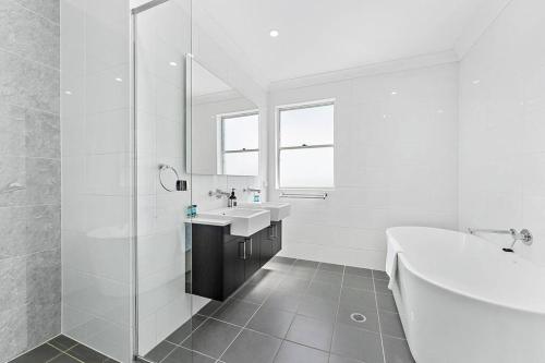 Baño blanco con bañera y lavamanos en AirCabin - Norwest - Luxury Lovely - 4 Beds House, en Baulkham Hills