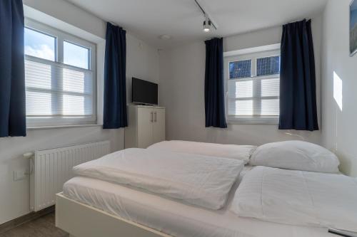 a white bed in a room with two windows at Ferienhaus Westwind Einzelhaus Westwind in Brösum