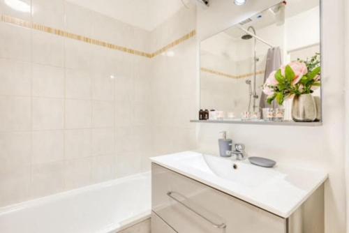 uma casa de banho branca com um lavatório, uma banheira e um espelho. em Le cosy DisneyLand Paris em Montévrain