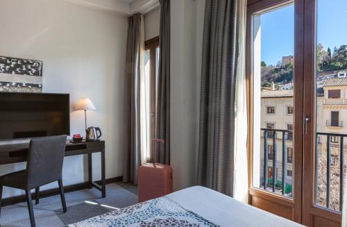 a hotel room with a bed and a desk and a window at Hotel Macià Plaza in Granada