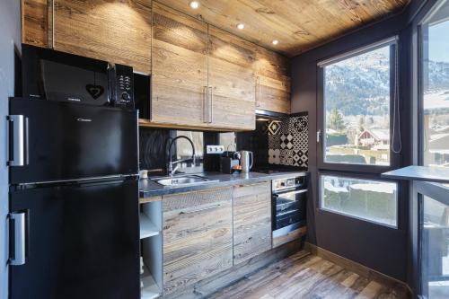 une cuisine avec un réfrigérateur noir et des armoires en bois dans l'établissement Le Nid d'Aigle - Modern Apartment Next to Ski lift Prarion - By Cozee Rentals, aux Houches