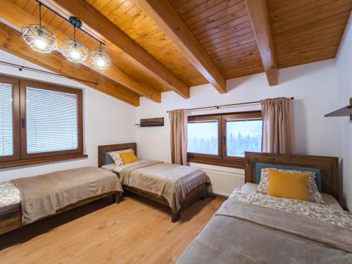 two beds in a room with windows and wooden ceilings at Chalety BUČINA in Oravská Lesná