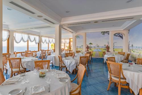 un ristorante con tavoli e sedie bianchi e l'oceano di Hotel Sporting a Vico Equense