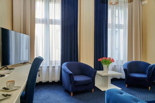 a room with blue chairs and a desk and a tv at Hotel Royal in Gliwice