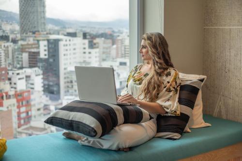 a woman sitting on a pillow with a laptop in a window at GO Quito Hotel in Quito