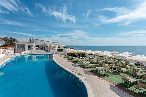 a pool with chairs and umbrellas next to the ocean at Hotel Cavalluccio Marino in Santa Marinella