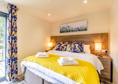 a bedroom with a large bed with a yellow blanket at Woodland Lakes Boutique Lodges 