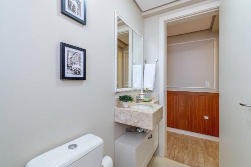 a bathroom with a sink and a toilet and a mirror at Café da Banca - Stay House Temporada in Gramado
