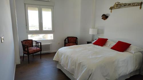 a bedroom with a white bed with red pillows and two chairs at ENTREOLIVOS in Jaén