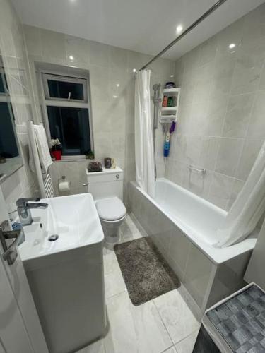 a white bathroom with a tub and a toilet and a sink at 2 Bedroom House - West London in Northolt