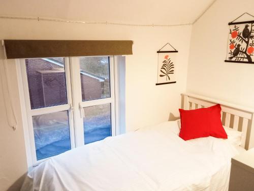 a bedroom with a bed with a red pillow and a window at Post Cottage in Hulland