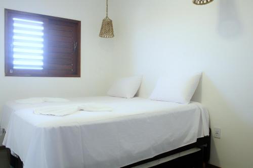 Cama blanca con sábanas blancas y ventana en Pousada Sal e Sol, en São Miguel do Gostoso