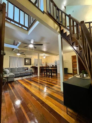 uma sala de estar em plano aberto com piso em madeira e uma escada em The Coral Casa em Caye Caulker