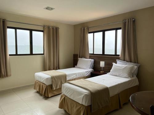 two beds in a hotel room with two windows at Pousada Da Serra in Bananeiras