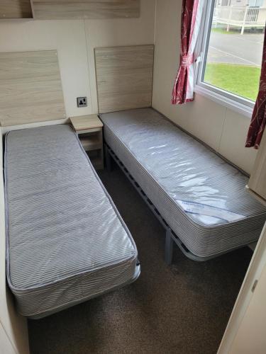 two beds in a small room with a window at Seawick Holiday Park in Saint Osyth